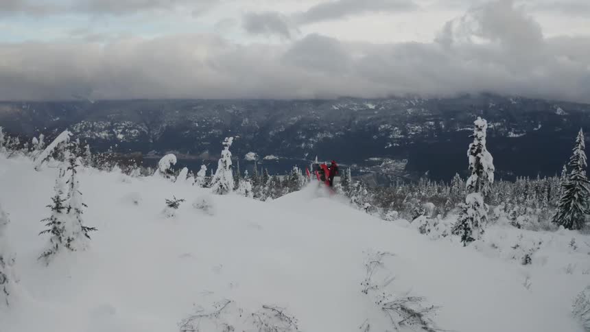 Person riding a snowmobile through tree covered hills