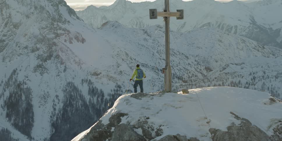 Person stands on a mountain top next to a cross