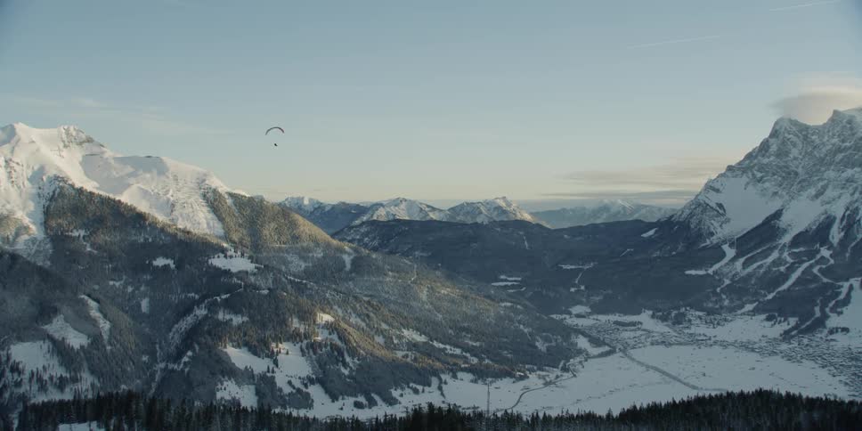 Paraglider floats over a snow covered mountain
