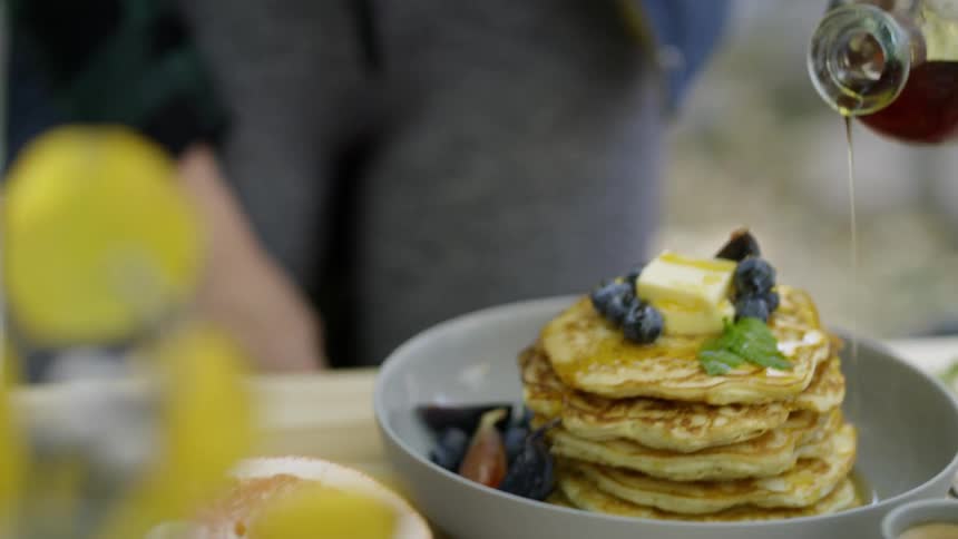 Person pours syrup on a stack of blueberry pancakes