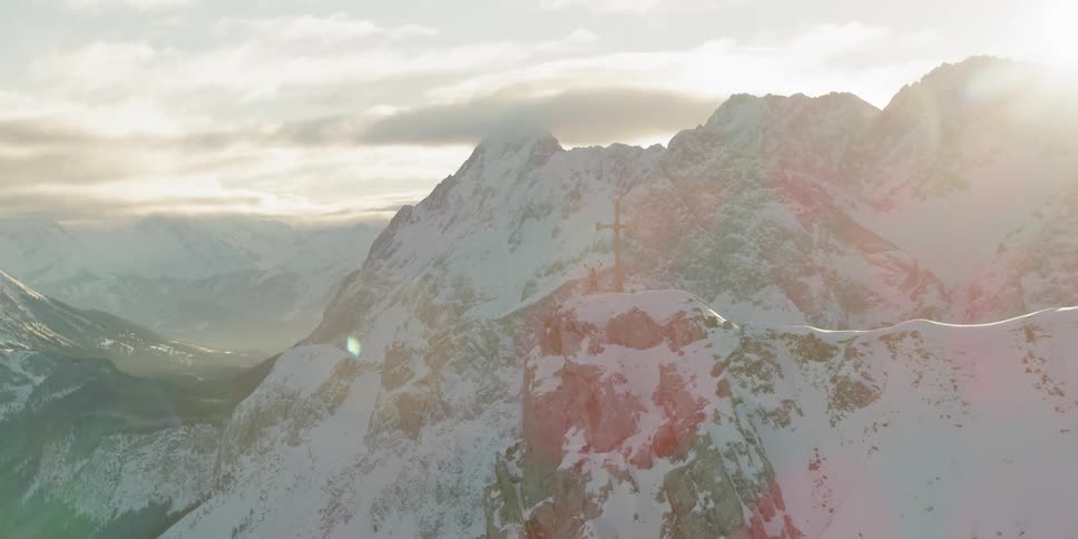 A person is standing by a cross on top of the mountain