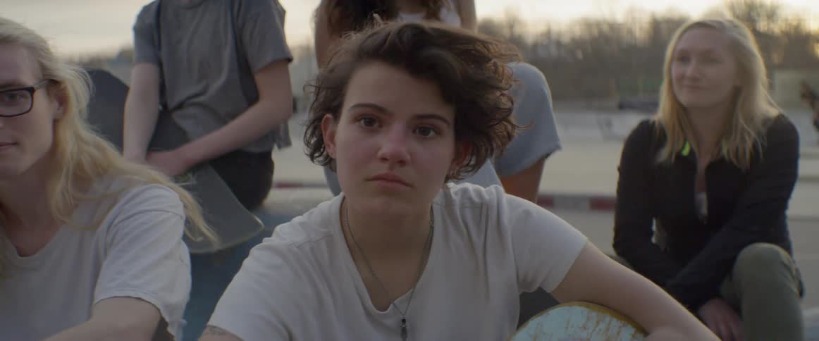 A woman sitting outside in a skate park rubs her face and looks up