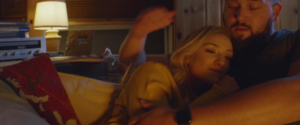 Man and woman sit on a couch cuddling at night