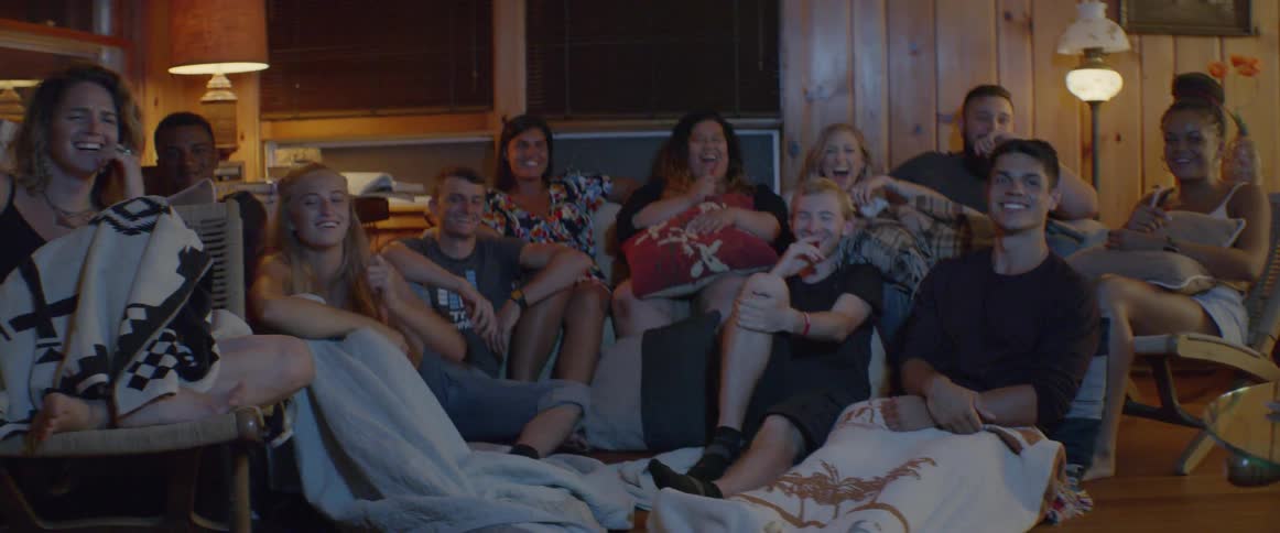 A group sit in the living room laughing at the television together