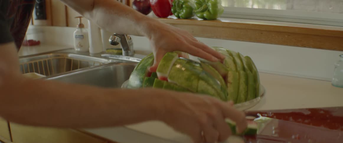 Man is placing watermelon slices on plate in kitchen