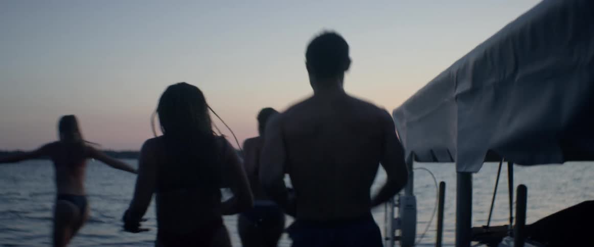 Group of people running and jumping into lake at sunset