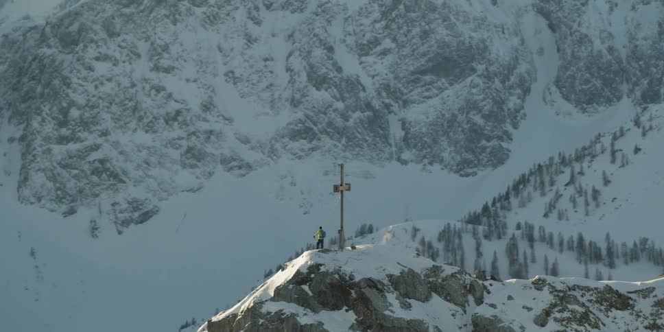 Person standing next to cross statue on top of snow covered mountain