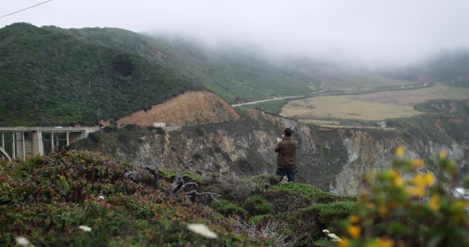 Man taking a picture of a cloud covered mountain