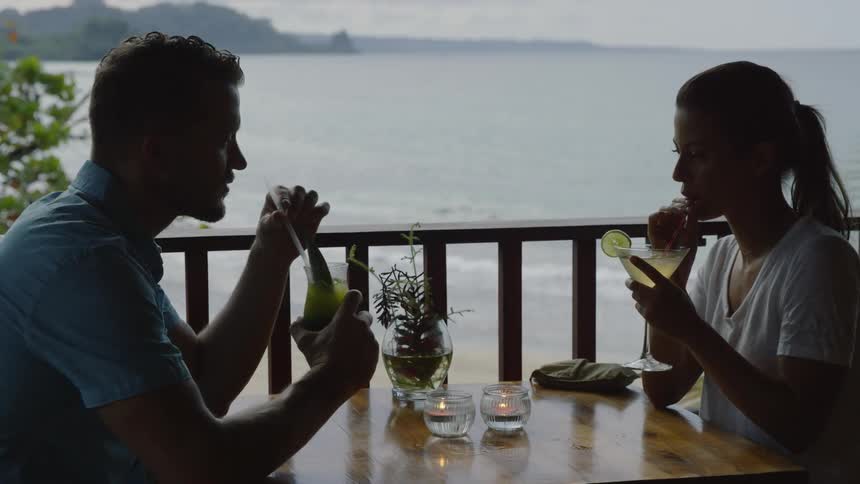 A man and woman drink cocktails on a beach patio