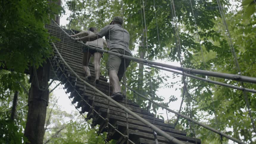 Two people climb a hanging bridge