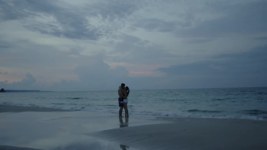 A couple embraces on the beach as waves come to shore