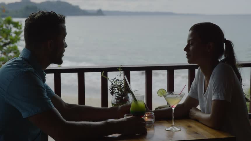 Two people sit at the table by the shore