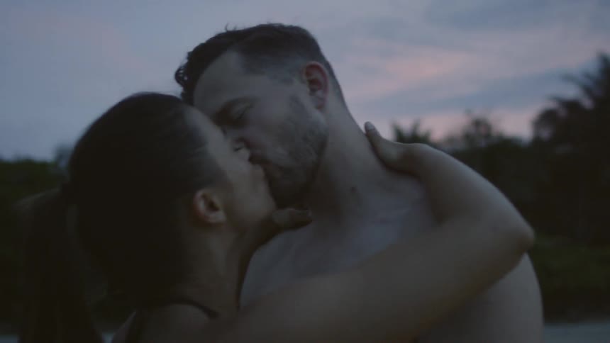 A man and woman hug and kiss by the shore