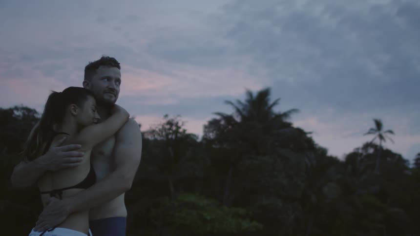 Man and woman in swim suits are embracing outside at sunset