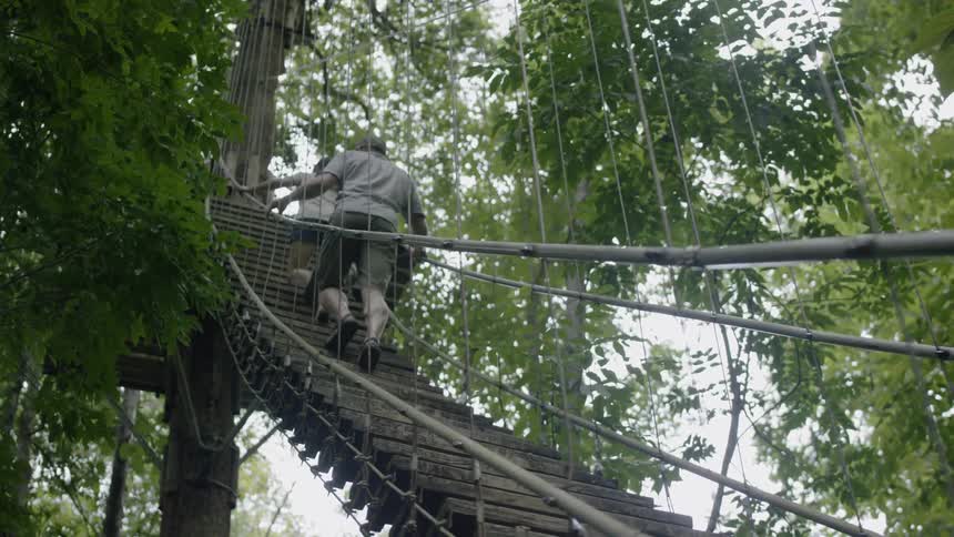 Man and woman walk across a swinging bridge in the forest