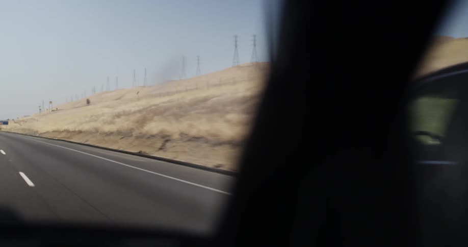 Vehicles driving down a road with hills on the side