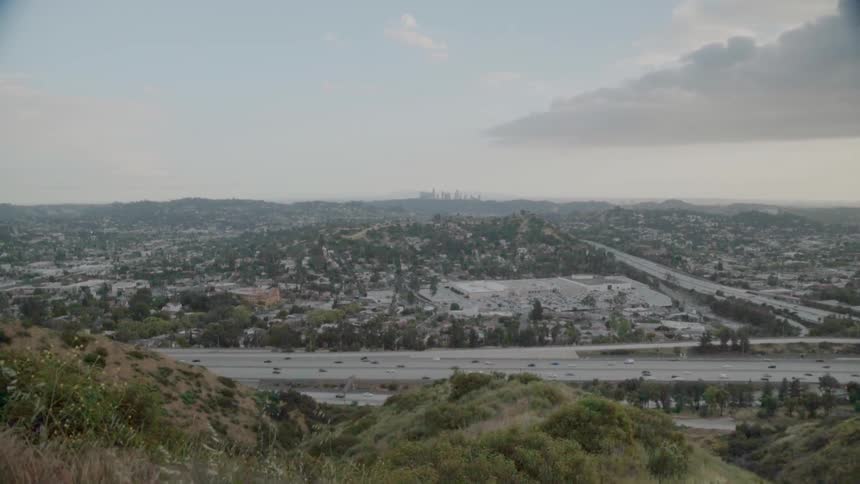 Traffic is flowing on a freeway in a hilly area on a cloudy day