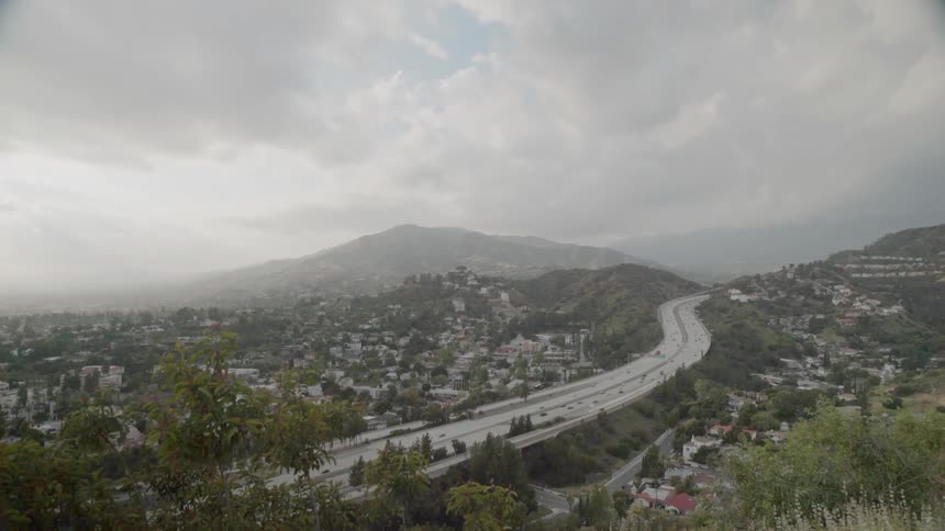 Traffic is flowing on a freeway in an hilly community in during daylight