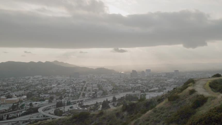 Traffic is flowing on a freeway in a hilly area on a cloudy day