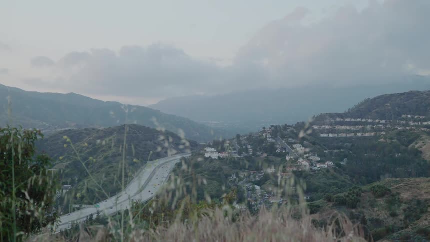 Traffic is flowing on a freeway through a valley during a cloudy day