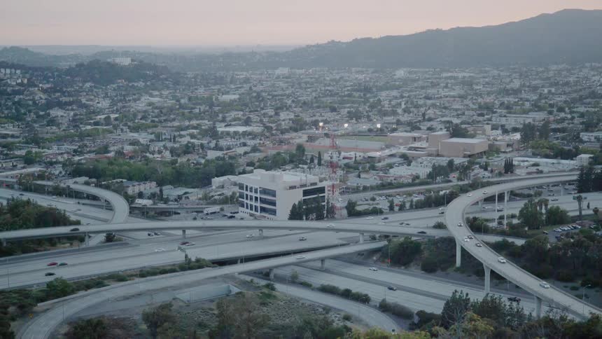 Traffic is flowing on a freeway system in an urban valley at dusk