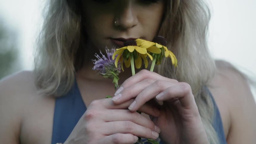 A woman is smelling a few flowers