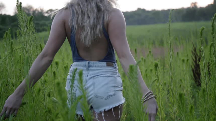 A woman walks through the tall grass with her arms stretched