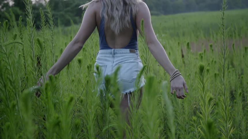 A woman is walking through a field of tall grass