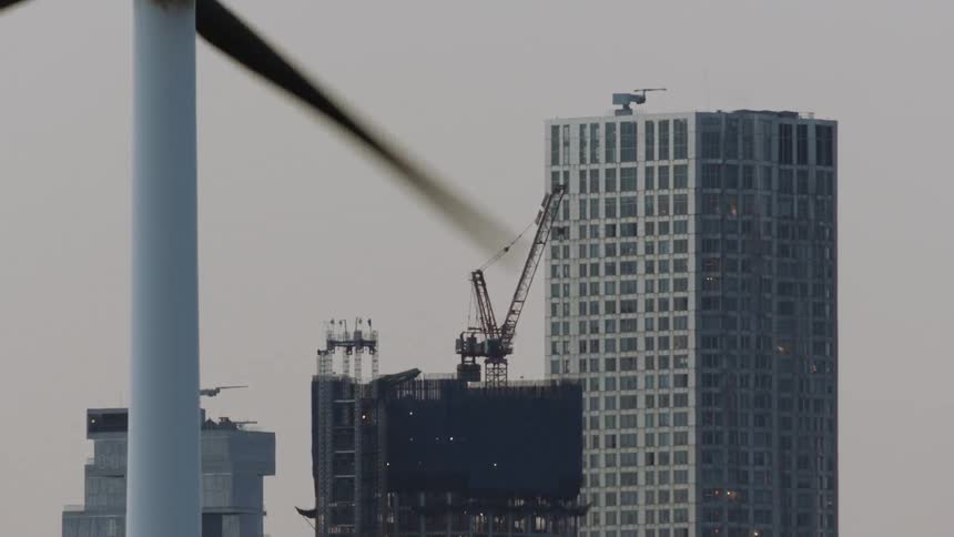 Blades of a wind turbine turn and a crane sits on a rooftop