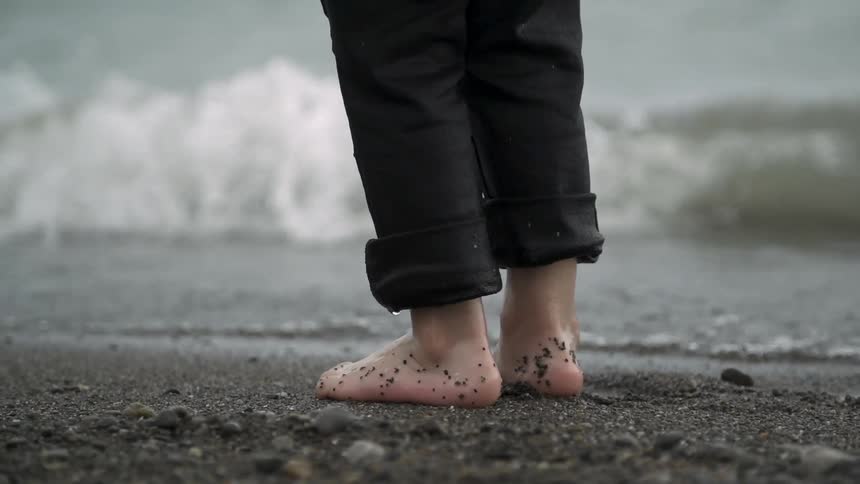 Water is dripping off of a child's pants as he stands near the waves on a beach