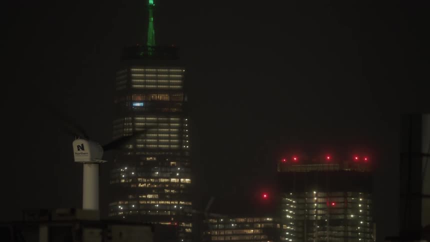 A large windmill runs on top of the city building at night