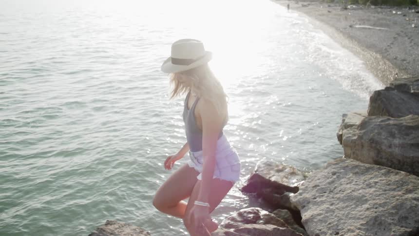 A woman at a beach is hopping from one rock to another in daylight