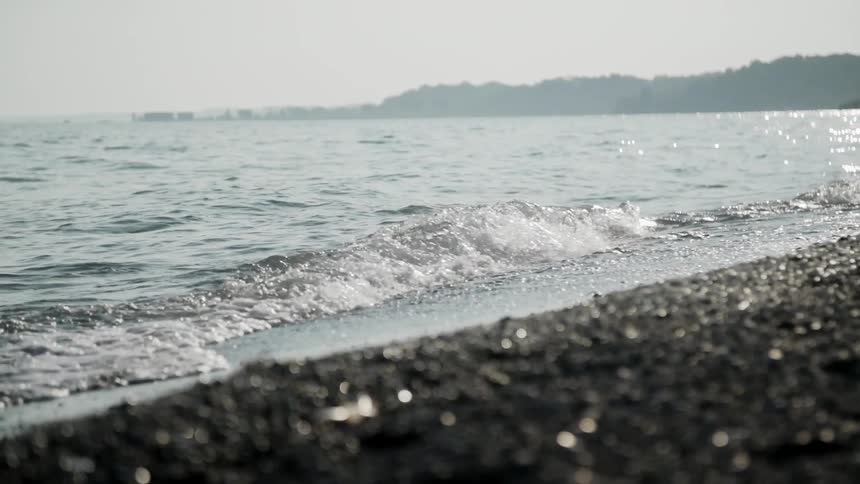 A wave is cresting and rolling onto a beach on a sunny day
