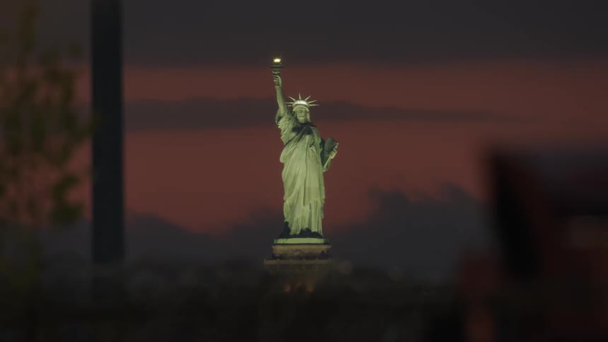 The statue of liberty is brightly lit at dawn