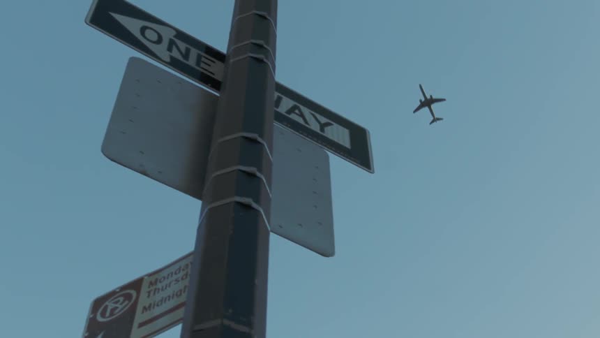 A plane flies above a street sign