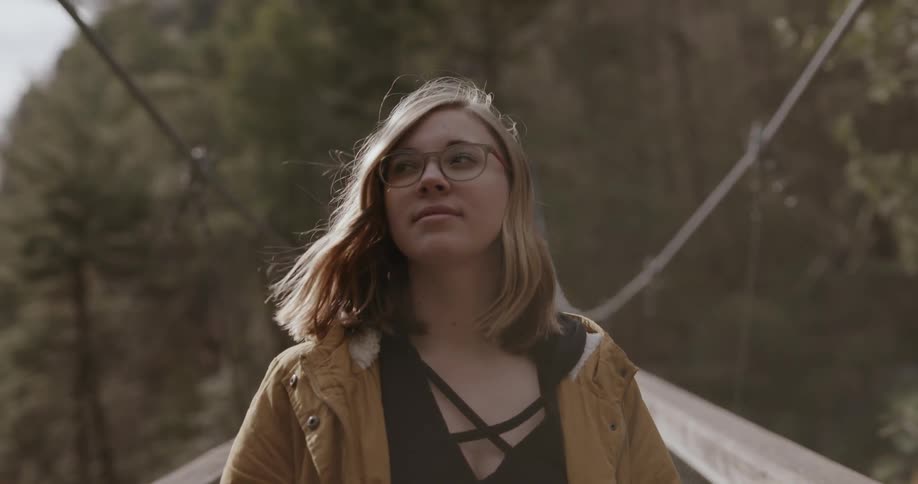 Woman wearing glasses walks across a swinging bridge