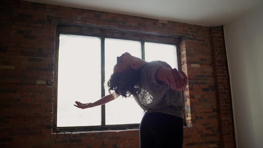 Woman bends backwards in an empty room with a window