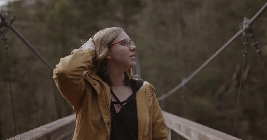 A woman is brushing back her hair as she walks across a bridge in a natural setting