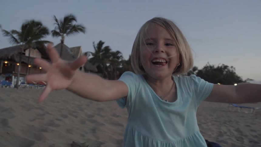 A girl smiles and chases the camera on a sandy beach