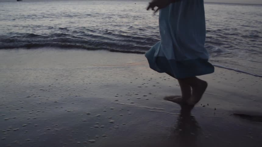 A person in a blue dress runs across the beach