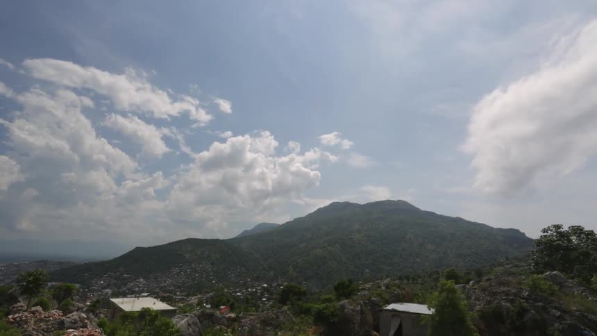 Time lapse of clouds blowing over mountains, a valley and some buildings