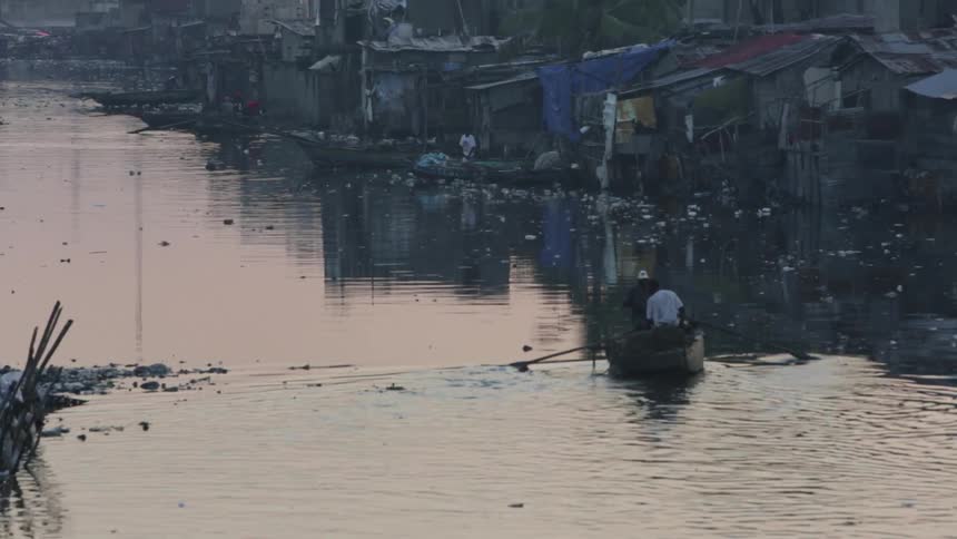 Two men in a paddle boat slowly move in the calm waters near a village