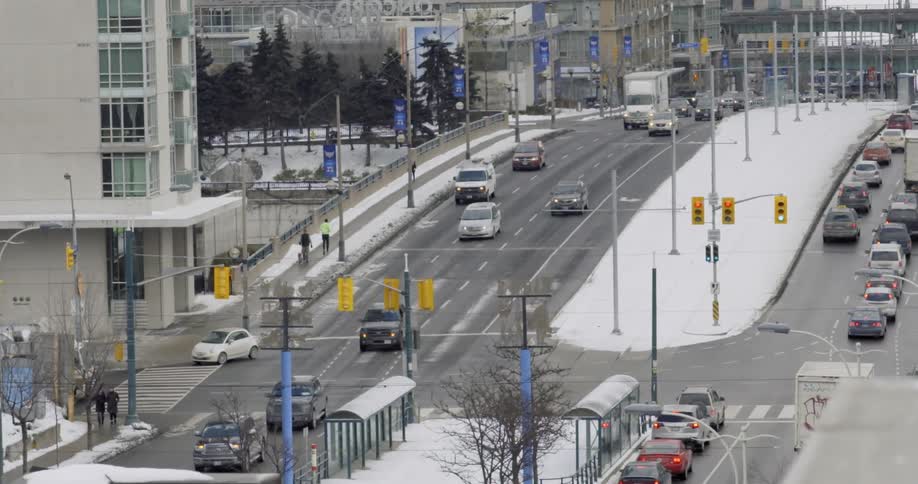View of traffic going down a hill in an urban area as it lightly snows