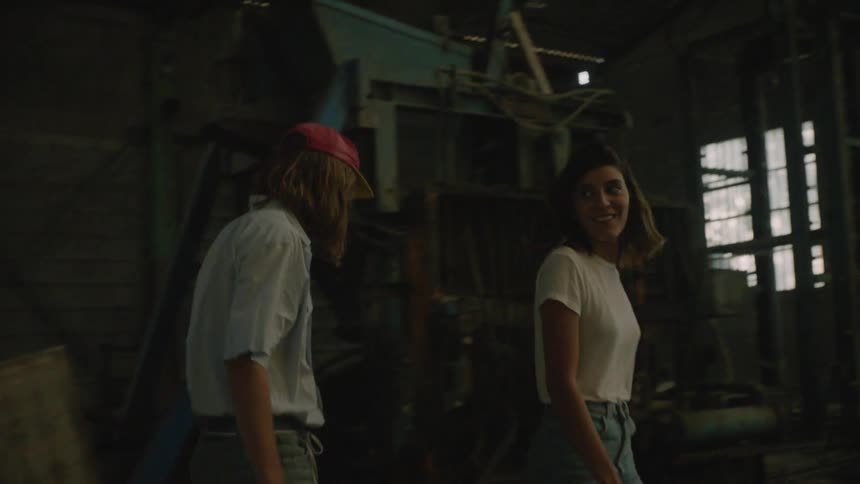 A man and woman walk around an abandoned building looking at equipment