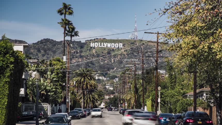 Cars drive up and down the road near the hollywood sign