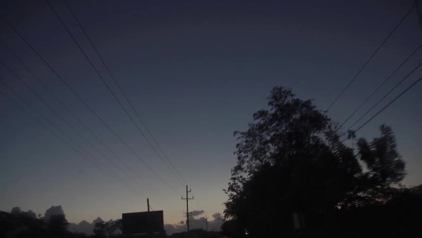 Power lines and trees line a road at sunset