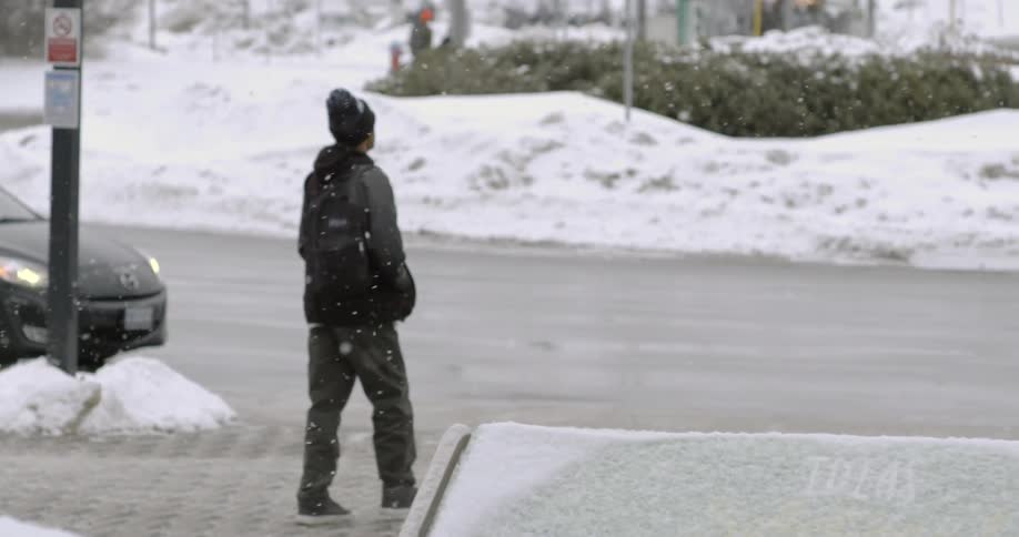 A kid with a backpack is walking down a street while its snowing