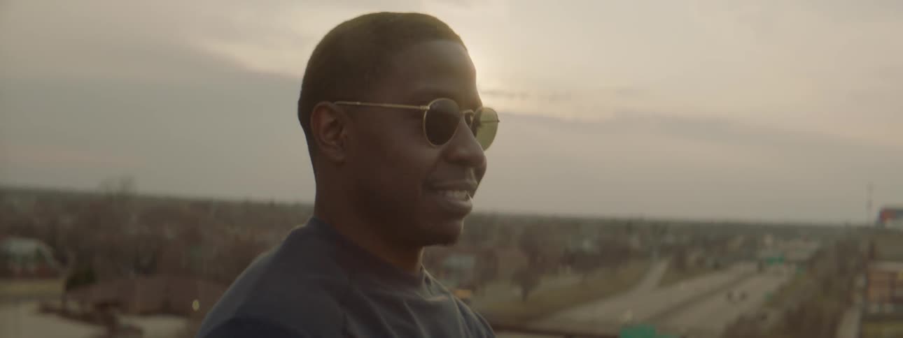 Smiling man wearing sunglasses stands outside with a highway below
