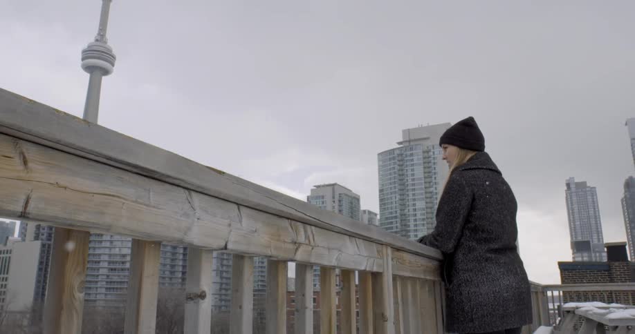 A woman looks over a wall as it lightly snows in an urban area