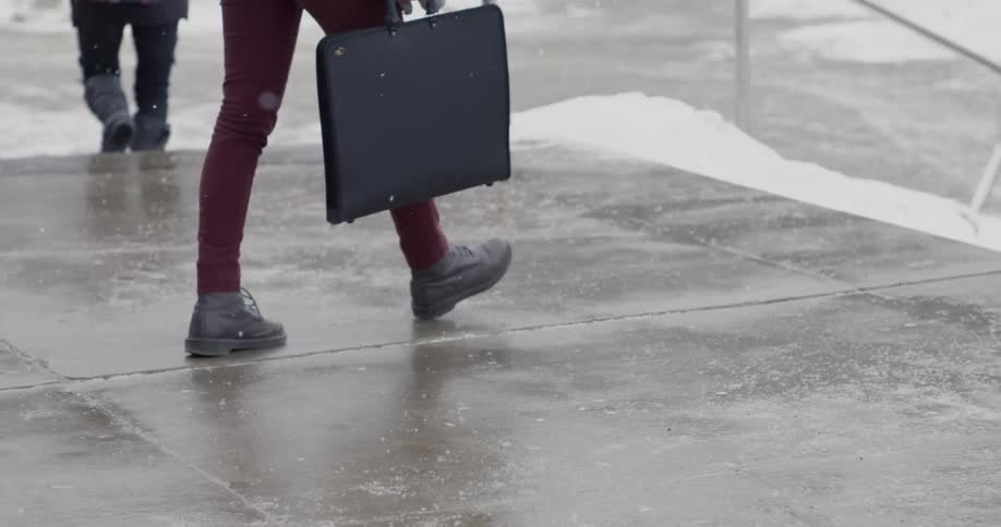 A man with a briefcase walks on concrete as it snows